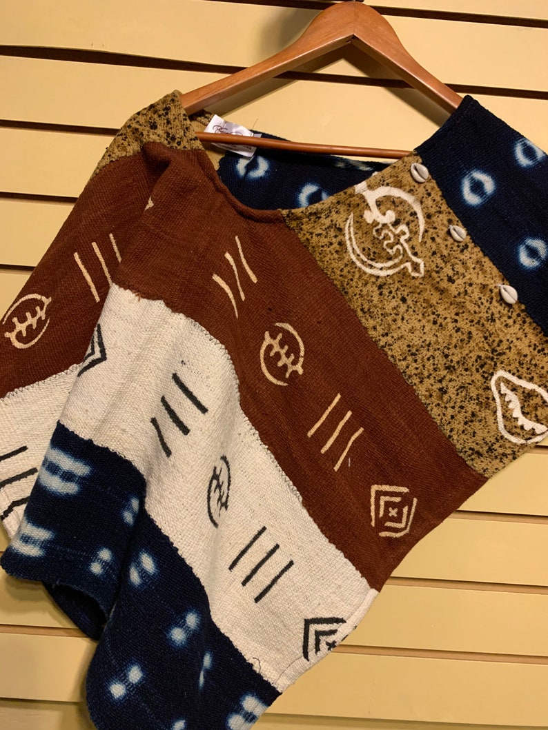 May include: A brown, tan, white, and blue patterned poncho with a button closure. The poncho has a geometric design with symbols and lines.