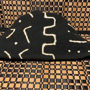 May include: Black and white patterned fabric hat with a geometric design. The hat is made of a woven material and has a rounded shape.