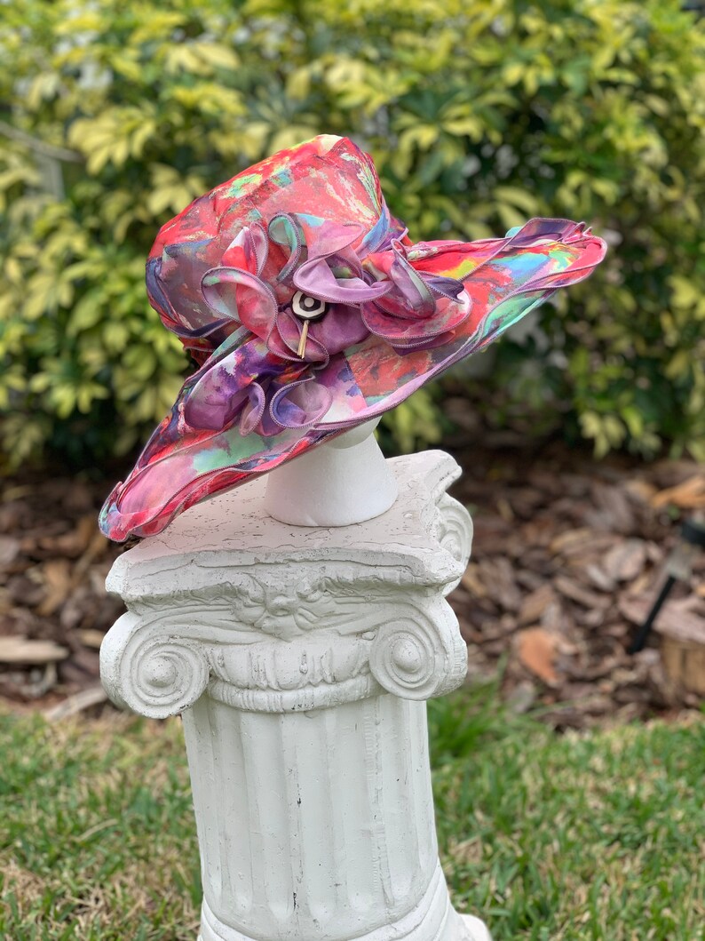 May include: A large, colorful hat with a floral print and a pink ruffle. The hat is made of a sheer fabric and has a wide brim.