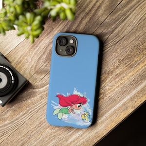 May include: A blue phone case with a cartoon image of Ariel from The Little Mermaid swimming with Flounder. The background is a watercolor-style design with blue, pink, and green colors.