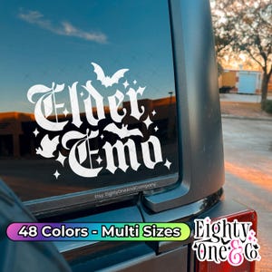 May include: A white vinyl decal applied to a vehicle window featuring the text Elder Emo in a gothic font, surrounded by small bat silhouettes and four-pointed star shapes. The text Etsy: EightyOneAndCompany is printed at the bottom edge.