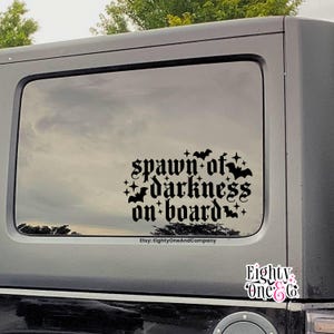 May include: Black vinyl car window decal with the text "spawn of darkness on board" in a gothic font, decorated with bats and stars. The Etsy shop name "EightyOneAndCompany" is at the bottom.