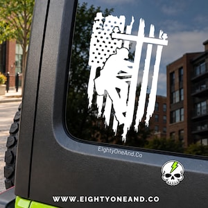 May include: A white vinyl decal featuring a stylized American flag with a lineman climbing a utility pole integrated into the design. The text EightyOneAnd.Co is visible below the decal, along with a small skull logo with a green lightning bolt.