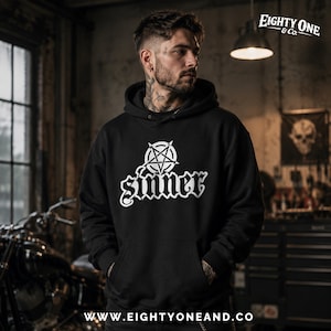 May include: Black hoodie with a white pentagram and the word "Sinner" in a gothic font. The hoodie has a front pocket and a hood. The brand name "Eighty One & Co." is visible in the top right corner. The website address is visible at the bottom.