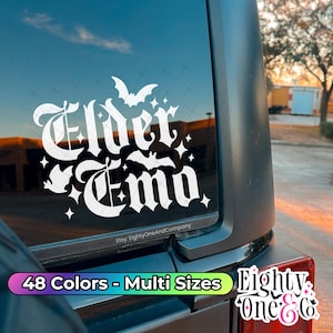 May include: White vinyl sticker with the text "Elder Emo" in a gothic font. The sticker features bats and stars. The sticker is on the back window of a black car. The text "48 Colors - Multi Sizes" is visible below the sticker. The text "Eighty One & Co." is visible in the lower right corner of the image.