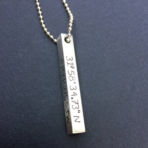 May include: Silver necklace with a rectangular pendant engraved with the coordinates "37.58.34.73" N 81.13.28.53" W.