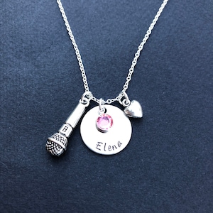May include: Silver necklace with a microphone charm, a small heart charm, and a round charm with a pink rhinestone and the name "Elena" engraved on it.