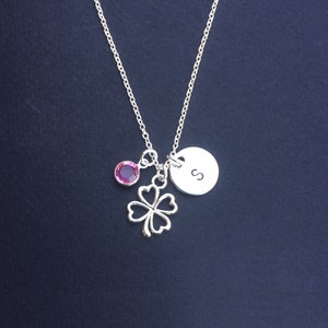 May include: Silver necklace with a four-leaf clover charm, a pink crystal, and a round charm with the letter "S" engraved on it.