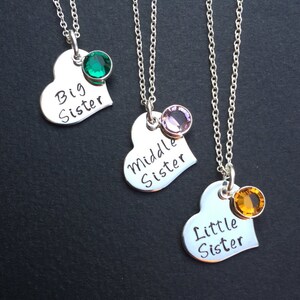May include: Three silver heart necklaces with different colored gemstones. The necklaces say "Big Sister", "Middle Sister", and "Little Sister".