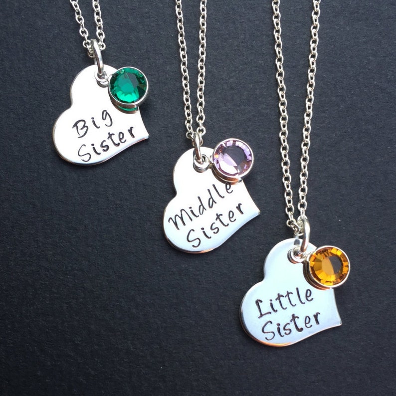 May include: Three silver heart necklaces with different colored gemstones. The necklaces say "Big Sister", "Middle Sister", and "Little Sister".