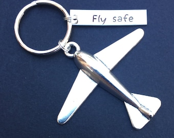 Może przedstawiać: Srebrny brelok do kluczy w kształcie samolotu ze srebrnym kółkiem i zawieszką z napisem "Fly safe".