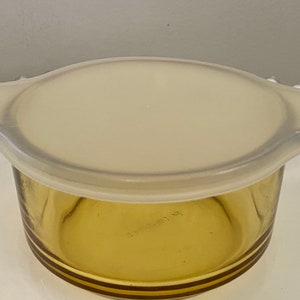 May include: A clear glass amber-colored baking dish with a white plastic lid. The dish has a rounded bottom and a slightly flared rim.