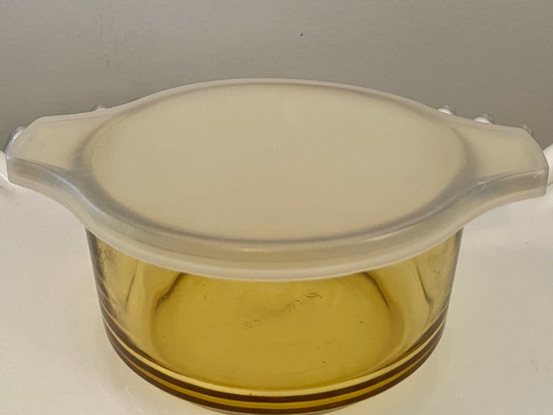 May include: A clear glass amber-colored baking dish with a white plastic lid. The dish has a rounded bottom and a slightly flared rim.