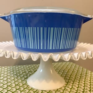 May include: Blue and white bar code patterned casserole dish with a glass lid, sitting on a white cake stand.
