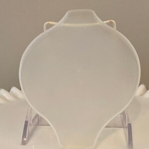 May include: A white, round, ceramic dish with a slightly curved edge. The dish is on a clear plastic stand.