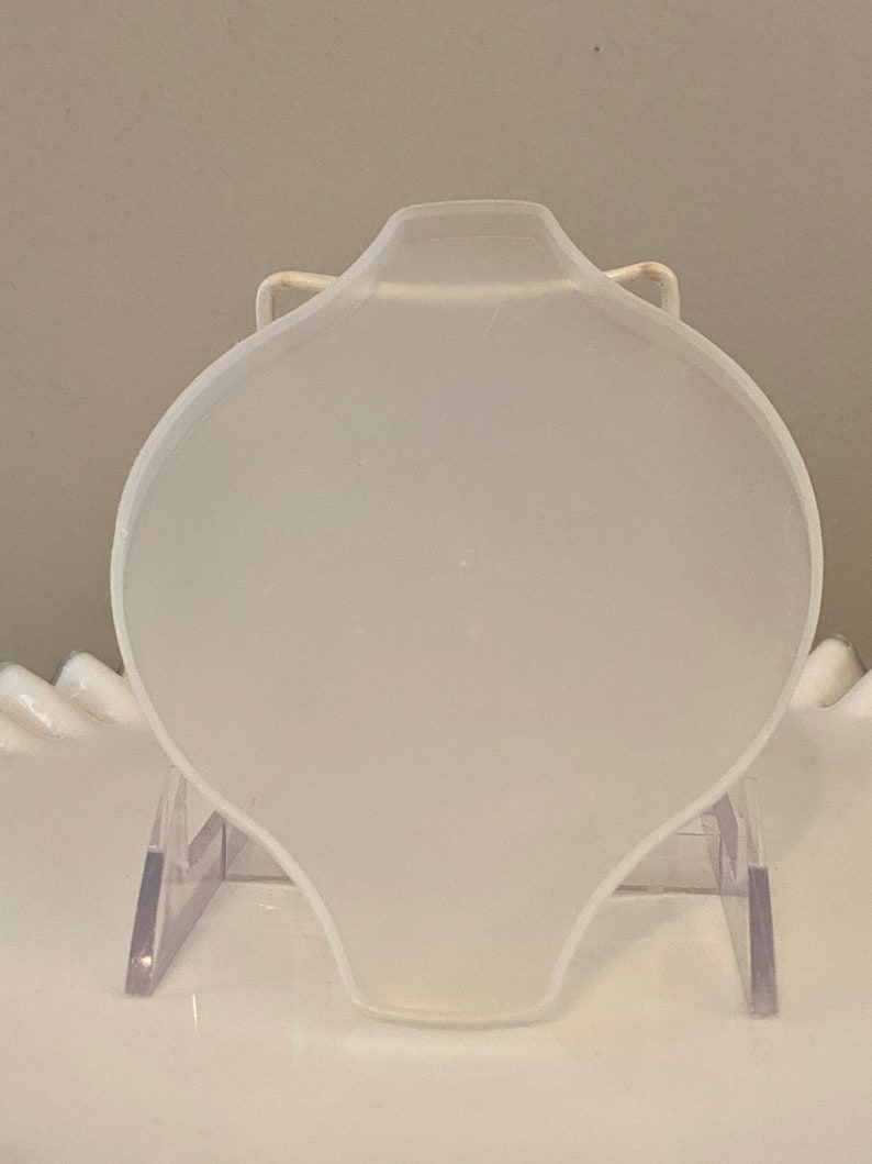 May include: A white, round, ceramic dish with a slightly curved edge. The dish is on a clear plastic stand.