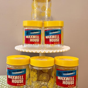 May include: A collection of clear glass storage containers with yellow lids. Some jars feature a yellow floral pattern. The labels read "Maxwell House Coffee" and "Free Storage Container Corning". Each jar is labeled "Net Wt. 10 oz."