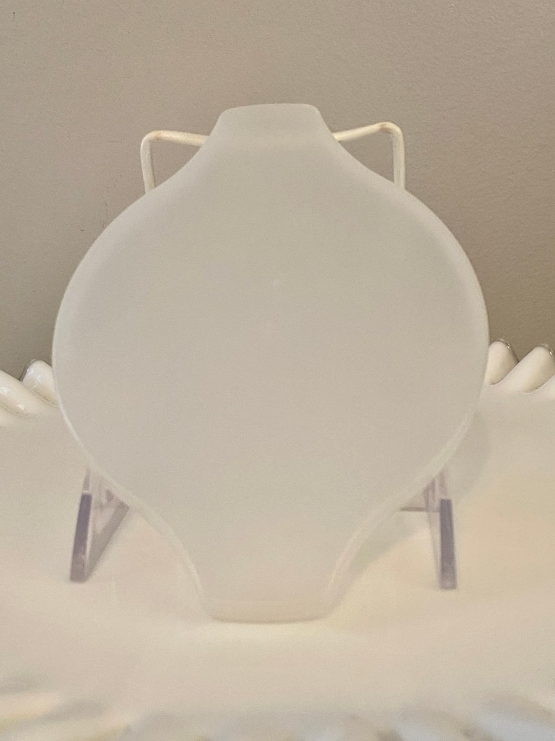 May include: A white frosted glass cake plate with a rounded edge and a smooth surface. The plate is on a clear plastic stand.