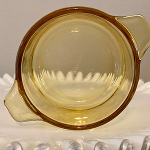May include: A yellow glass baking dish with two handles. The dish is empty and has a slight curve to the bottom.