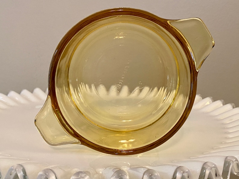 May include: A yellow glass baking dish with two handles. The dish is empty and has a slight curve to the bottom.