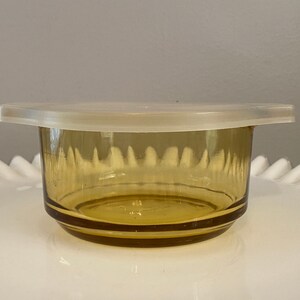 May include: A small amber glass bowl with a white plastic lid. The bowl has a textured design and is perfect for storing small items.