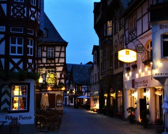 May include: A street scene at night in a European town with half-timbered buildings. The street is lined with shops and restaurants, including one called "Altes Haus" and another called "Hotel am Markt".
