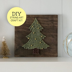 May include: DIY string art craft kit featuring a Christmas tree design. The tree is made of green string on a dark wood square, adorned with gold beads. The kit includes the text "DIY STRING ART CRAFT KIT" in a yellow circle.