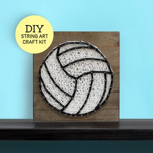May include: A square wooden board featuring a volleyball design created with white and black string art. A yellow circular label in the upper left corner displays the text DIY STRING ART CRAFT KIT in black capital letters.