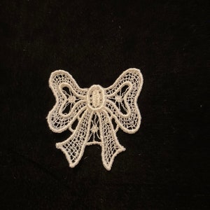 May include: A white lace bow with intricate details, ideal for adding a touch of elegance to crafts and projects.