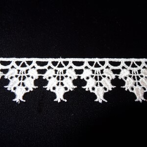 May include: White lace trim with a delicate floral design. The trim features a scalloped edge and a repeating pattern of small flowers.