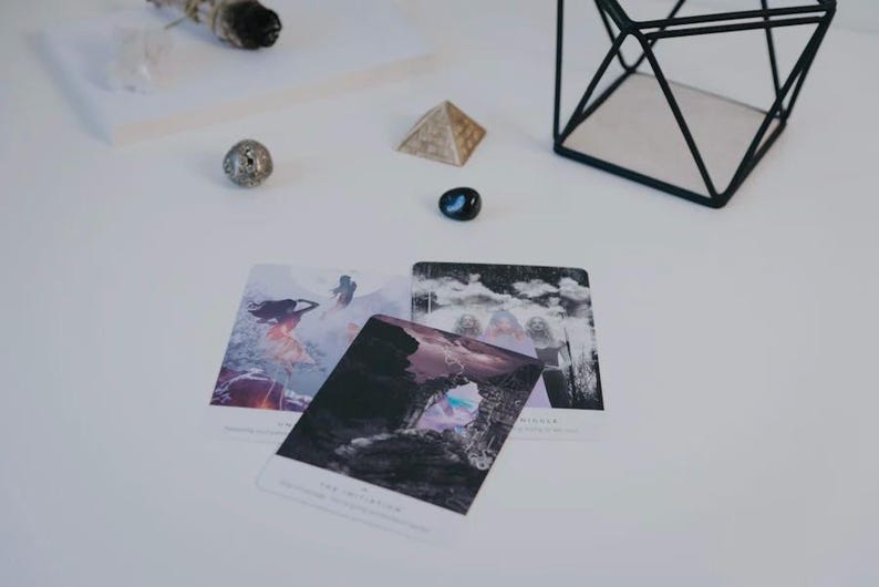 Op de afbeelding: Drie tarotkaarten op een wit oppervlak. De kaarten zijn wit met zwarte en grijze afbeeldingen. De kaarten zijn getiteld "De Magier", "De Wereld" en "De Geliefden".