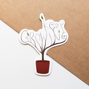 May include: A white sticker with a brown plant growing out of a red pot. The plant is shaped like the words "Keep Growing".