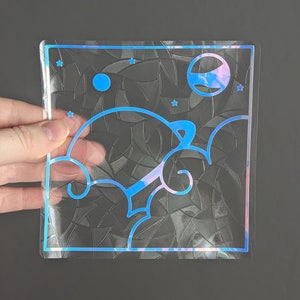 May include: A clear iridescent sticker with a blue outline. The sticker features a spaceship flying through clouds with a planet and stars in the background.