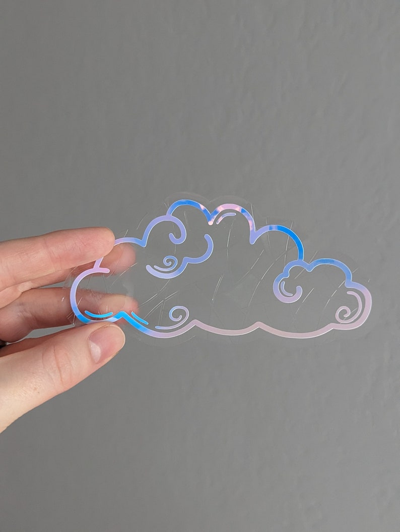 May include: A clear iridescent sticker with a blue and pink outline of a cloud. The cloud has a whimsical, cartoon-like design.