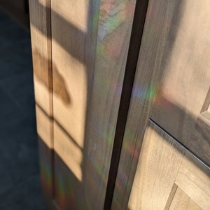 May include: Close-up of a wooden cabinet door with a rainbow-like reflection of light shining through the grain of the wood.