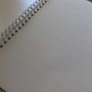 May include: A white spiral bound notebook with a silver binding.