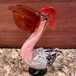 May include: A glass pelican figurine with a red head, white and black speckled body, and a black base.