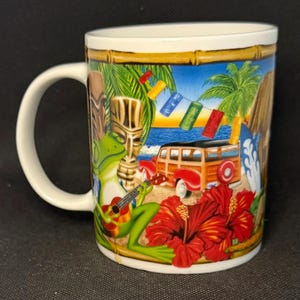 K&ouml;nnte beinhalten: Ein wei&szlig;er Keramikbecher mit einer farbenfrohen tropischen Szene, die einen gr&uuml;nen Frosch beim Gitarrespielen, eine h&ouml;lzerne Tiki-Statue, einen roten Kombi, Palmen, rote Hibiskusbl&uuml;ten und eine Lichterkette mit kleinen Tiki-Masken zeigt.