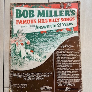 Op de afbeelding: Een vintage boekomslag in rood, wit en blauw. De titel is "Bob Miller's Famous Hill-Billy Songs" en bevat het lied "Answer to 21 Years". De omslag toont een cartoonillustratie van een man die viool speelt.