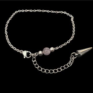 May include: Silver-toned bracelet with a delicate chain, a small, round, light purple bead, and a pointed cone charm. The bracelet has a lobster clasp closure and an adjustable chain. The jewelry is set against a black background.