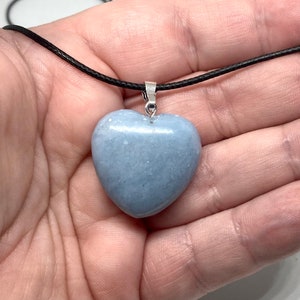 K&ouml;nnte beinhalten: Halskette mit hellblauem herzf&ouml;rmigem Anh&auml;nger. Der Anh&auml;nger besteht aus einem glatten, polierten Stein und h&auml;ngt an einer schwarzen Kordel. Der Anh&auml;nger ist etwa 3,8 cm breit.