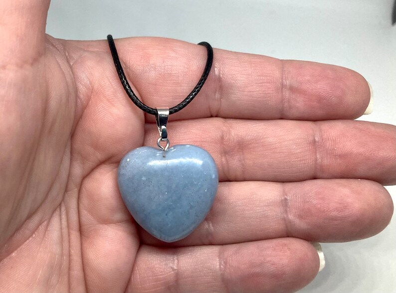 K&ouml;nnte beinhalten: Halskette mit hellblauem herzf&ouml;rmigem Anh&auml;nger. Der Anh&auml;nger besteht aus einem glatten, polierten Stein und h&auml;ngt an einer schwarzen Kordel. Die Halskette hat einen silberfarbenen Metallverschluss.