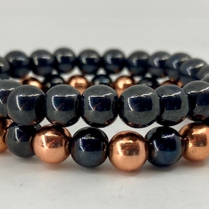 May include: Two bracelets made of black and copper beads. The top bracelet is made of black beads and the bottom bracelet is made of black and copper beads.
