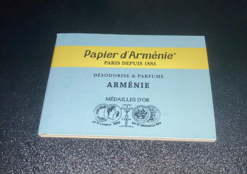 May include: A blue and yellow booklet with the text "Papier d'Arm&eacute;nie" and "Paris Depuis 1885". The booklet also says "D&eacute;sodorise & Parfume Arm&eacute;nie" and "M&eacute;dailles d'Or".
