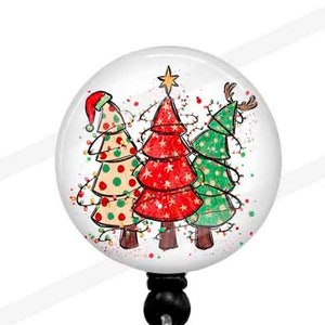 May include: A round Christmas-themed badge reel featuring three decorated Christmas trees. The trees are in red, green, and yellow with festive lights and a star on top. The reel has a black bead and a clear plastic clip.