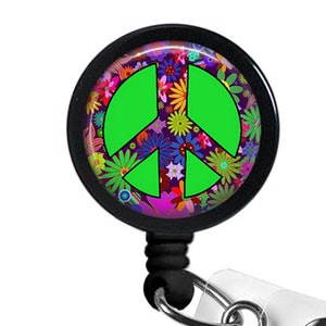 May include: A black retractable badge reel with a peace sign. The peace sign is bright green and set against a floral background of pink, purple, and yellow flowers. The reel has a clear plastic strap and a metal clip.