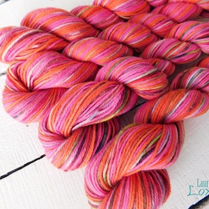May include: Close-up of a skein of pink, orange, and green yarn. The yarn is striped and has a variegated color pattern.