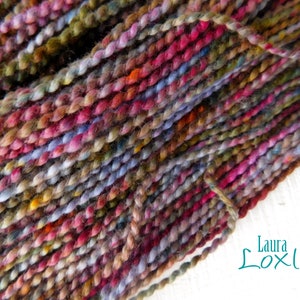May include: Close-up of hand-dyed yarn in a variety of colors, including pink, purple, green, and brown. The yarn is tightly twisted, creating a textured appearance. The image is of a skein of yarn, perfect for knitting or crocheting projects.