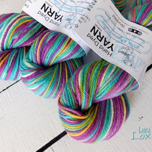 May include: Two skeins of hand-dyed yarn in a multi-colored pattern of teal, purple, yellow, and white. The yarn is labeled "100% Organic Cotton" and "Hand Dyed Yarn".