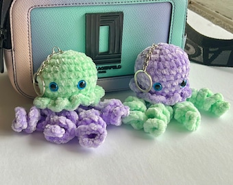 May include: Two crocheted octopus keychains with blue eyes. One octopus is green and the other is purple.